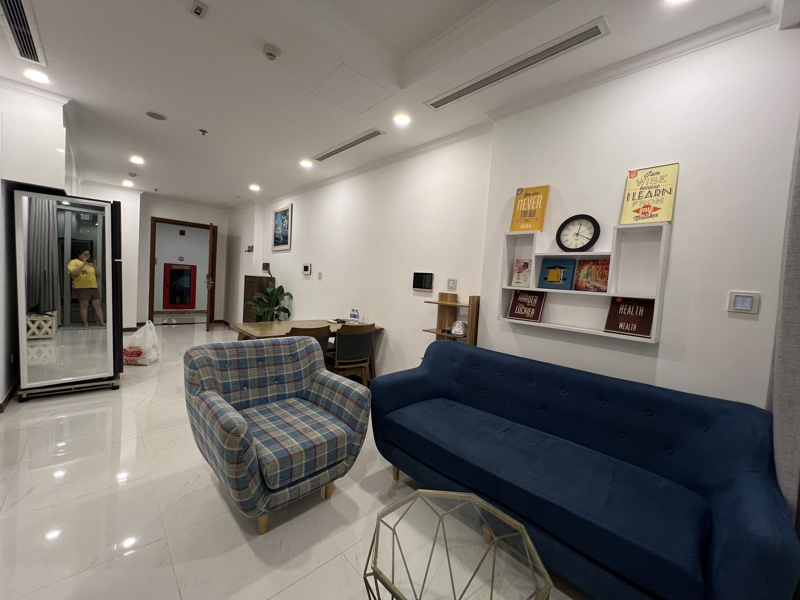 A modern living room with a blue sofa, plaid armchair, and a glass coffee table.