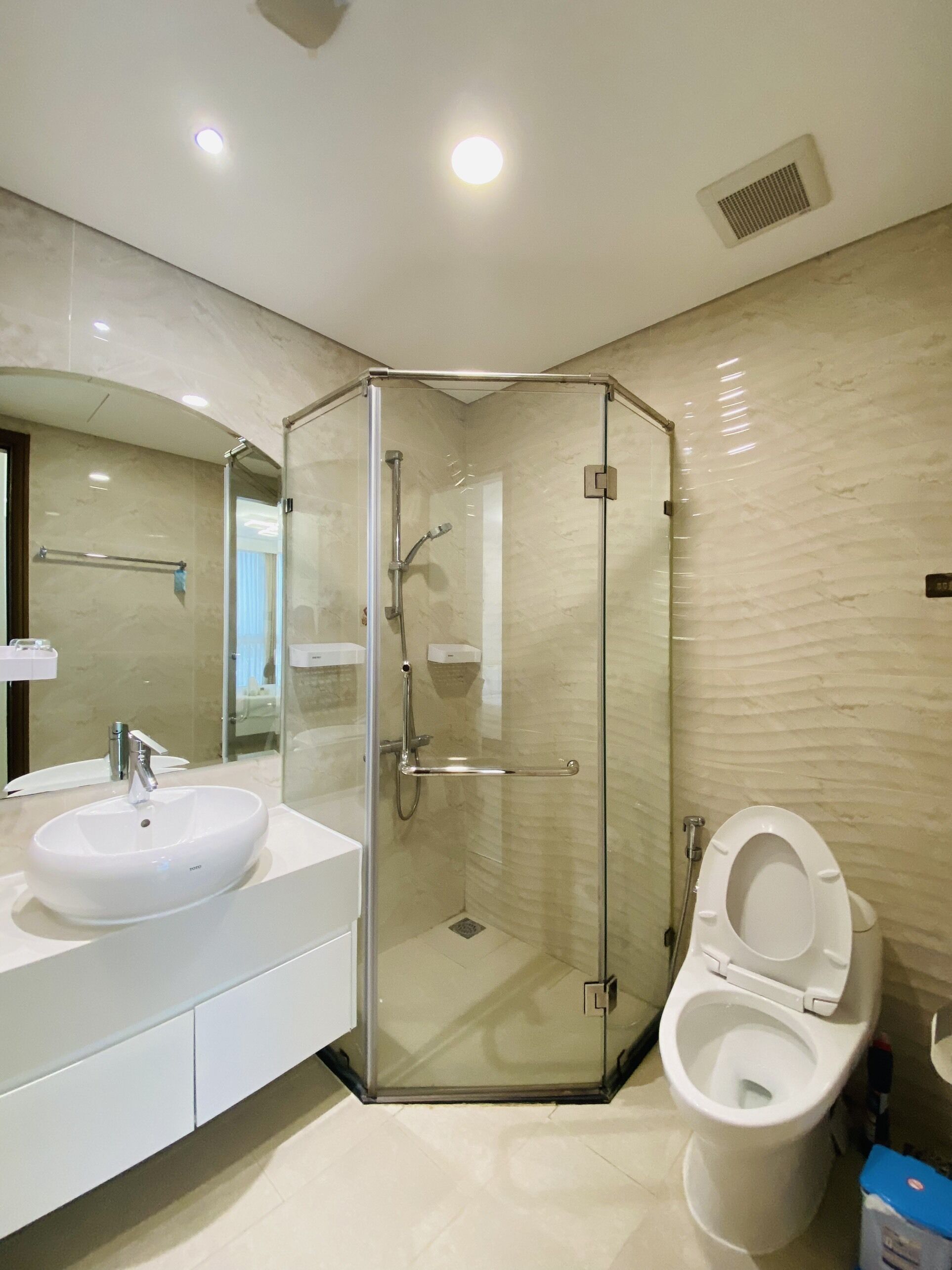 A modern bathroom with a glass-enclosed shower, a white sink, and a toilet.