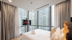 Una habitación de hotel moderna con una cama grande, un televisor de pantalla plana en la pared y vistas a altos edificios a través de amplios ventanales.