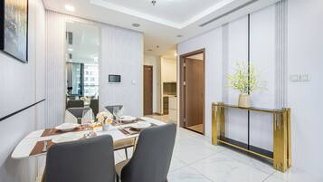 Un comedor moderno con una mesa blanca dispuesta para dos personas, un espejo grande y una consola con un florero de flores amarillas.