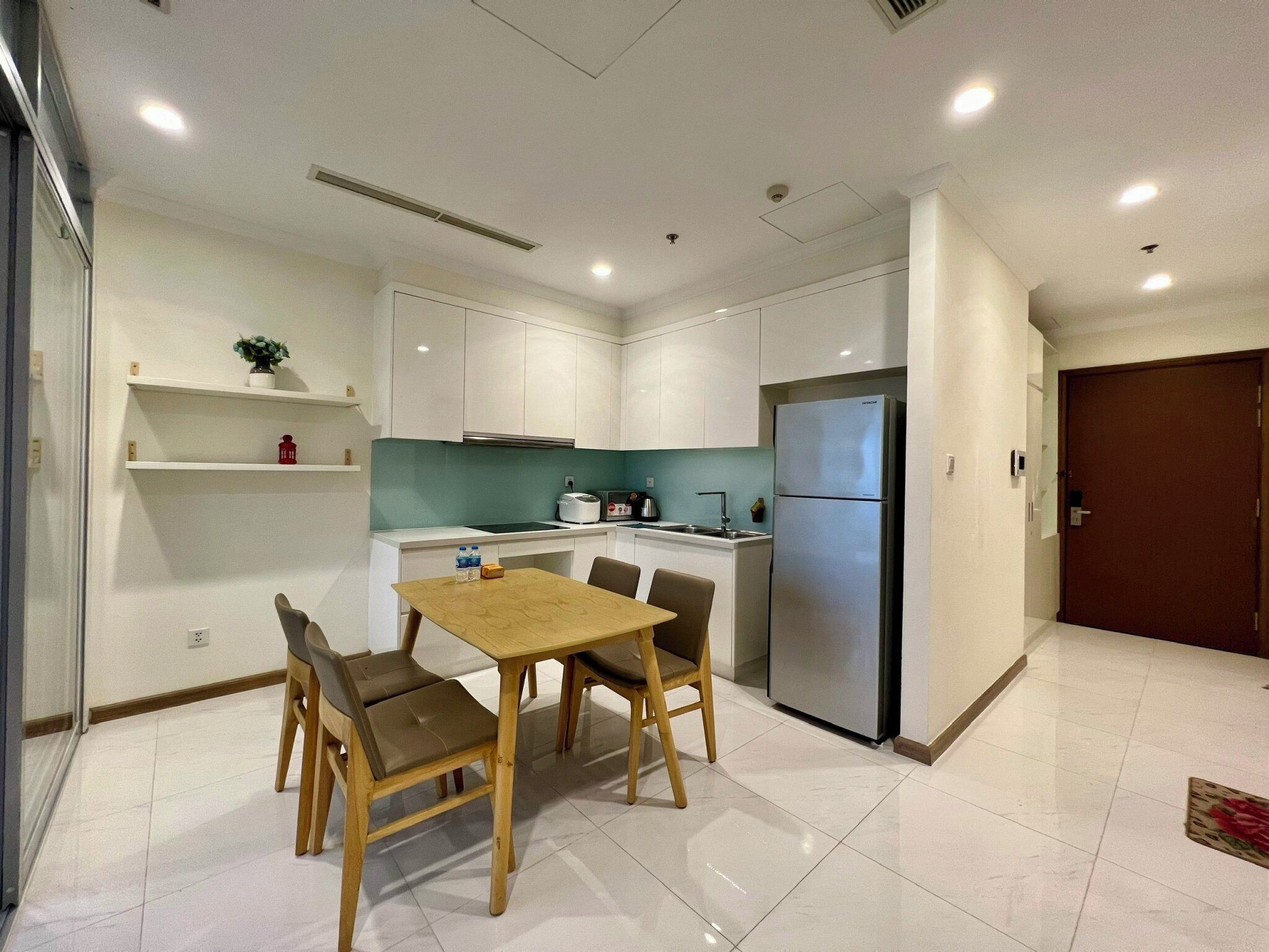 Una cocina moderna con armarios blancos, un refrigerador de acero inoxidable y una zona de comedor con mesa y sillas de madera.