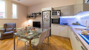 Eine moderne Küche mit eingebauter Mikrowelle, Backofen und Kühlschrank. Im Wohnbereich befindet sich ein Esstisch mit Stühlen sowie eine Couch.