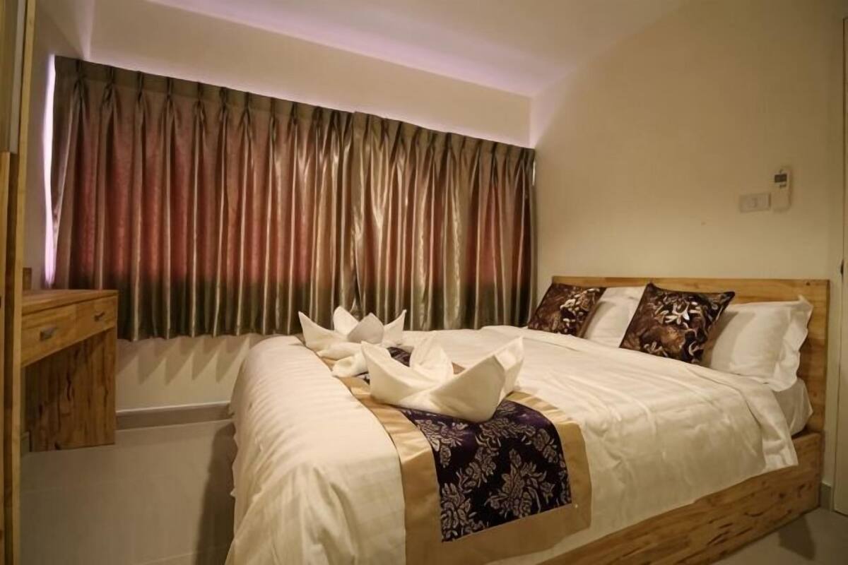 A neatly made bed with a wooden headboard, a bedside table, and a window with curtains.