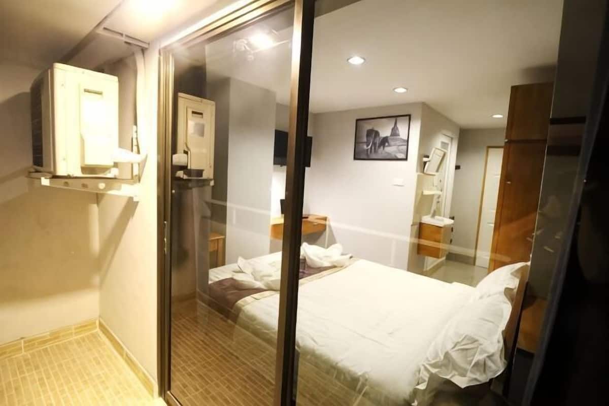 A hotel room with a bed, a glass shower enclosure, a bedside table, and a mirror.