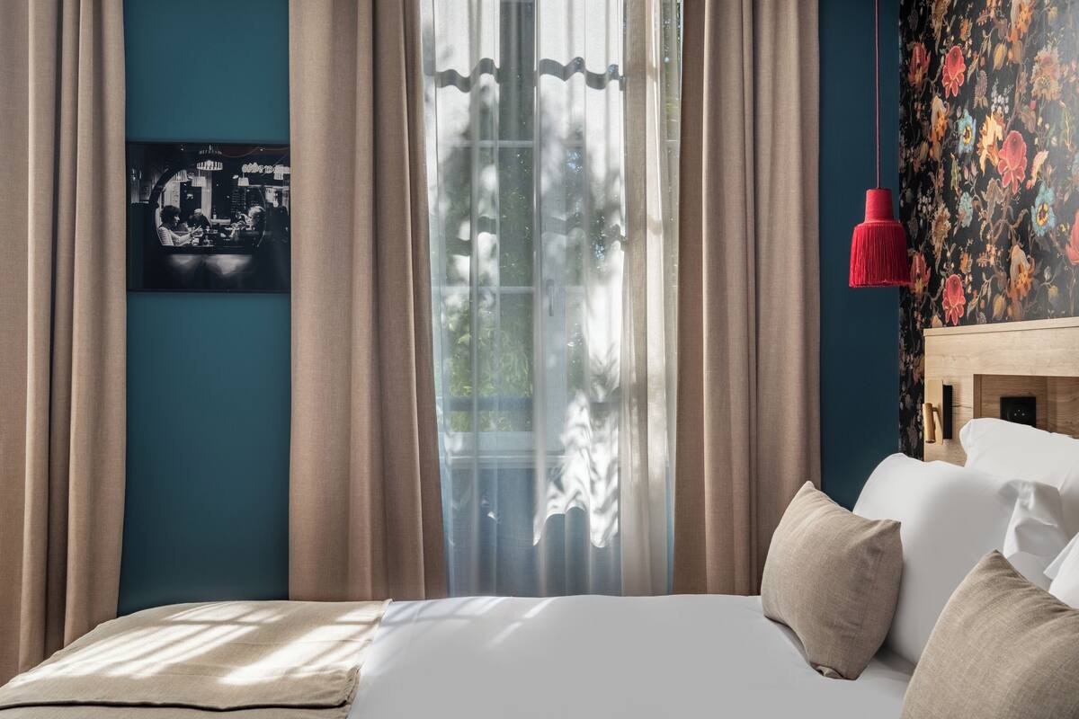Ein Schlafzimmer mit einem Bett, Vorhängen, einer roten Hängeleuchte und floralem Wandpapier.