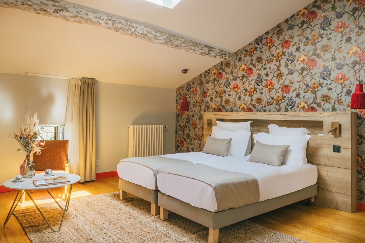 A bedroom with a large bed, a small table with a vase, a chair, and a radiator.