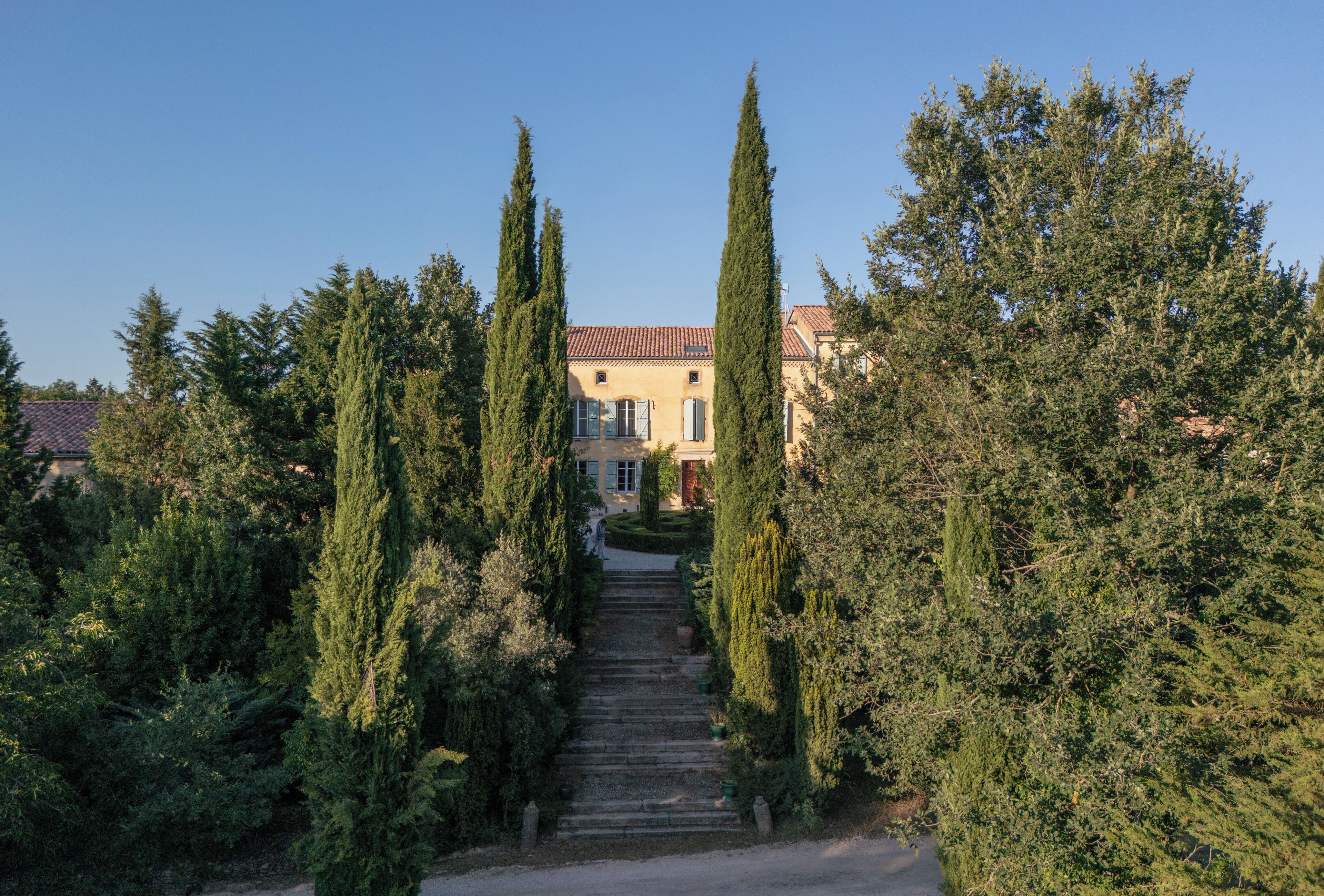 A stone staircase leading to a building with a red-tiled roof, surrounded by tall cypress trees.