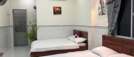 Una camera d'albergo con due letti singoli, un piccolo tavolo con un vaso di fiori, un condizionatore d'aria a parete e una porta decorativa.