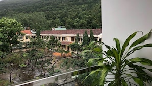 A view of a building with a red roof, surrounded by lush greenery and hills in the background. - Sunny Homestay Quy Nhon (Quy Nhon Nam)