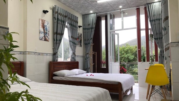 A bedroom with two beds, a large window, and a balcony with a yellow chair. - Sunny Homestay Quy Nhon (Quy Nhon Nam)