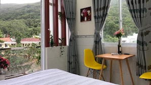 A bedroom with a bed, a small table, two chairs, and a window with curtains. - Sunny Homestay Quy Nhon (Quy Nhon Nam)