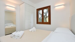 Une chambre à coucher avec un lit, un grand miroir, une armoire et une fenêtre donnant sur des arbres.