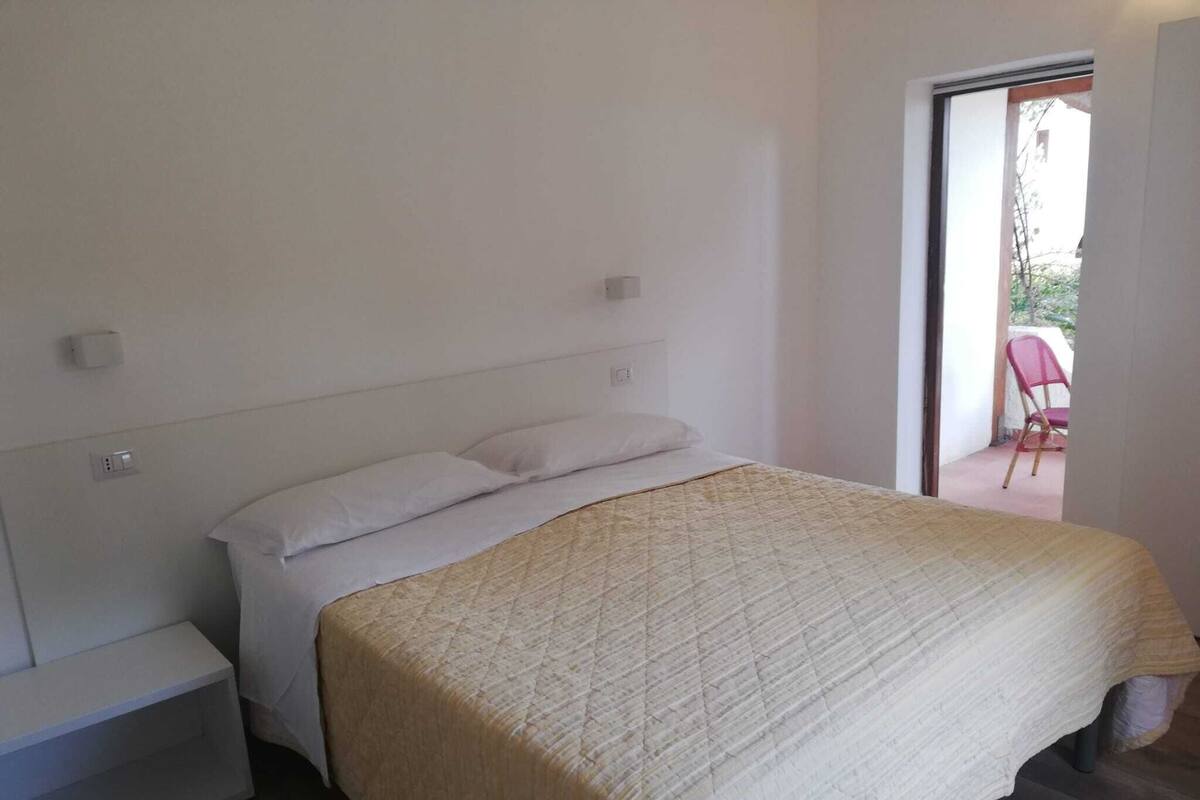Une chambre à coucher comprenant un lit, une table de chevet et donnant sur un espace extérieur.