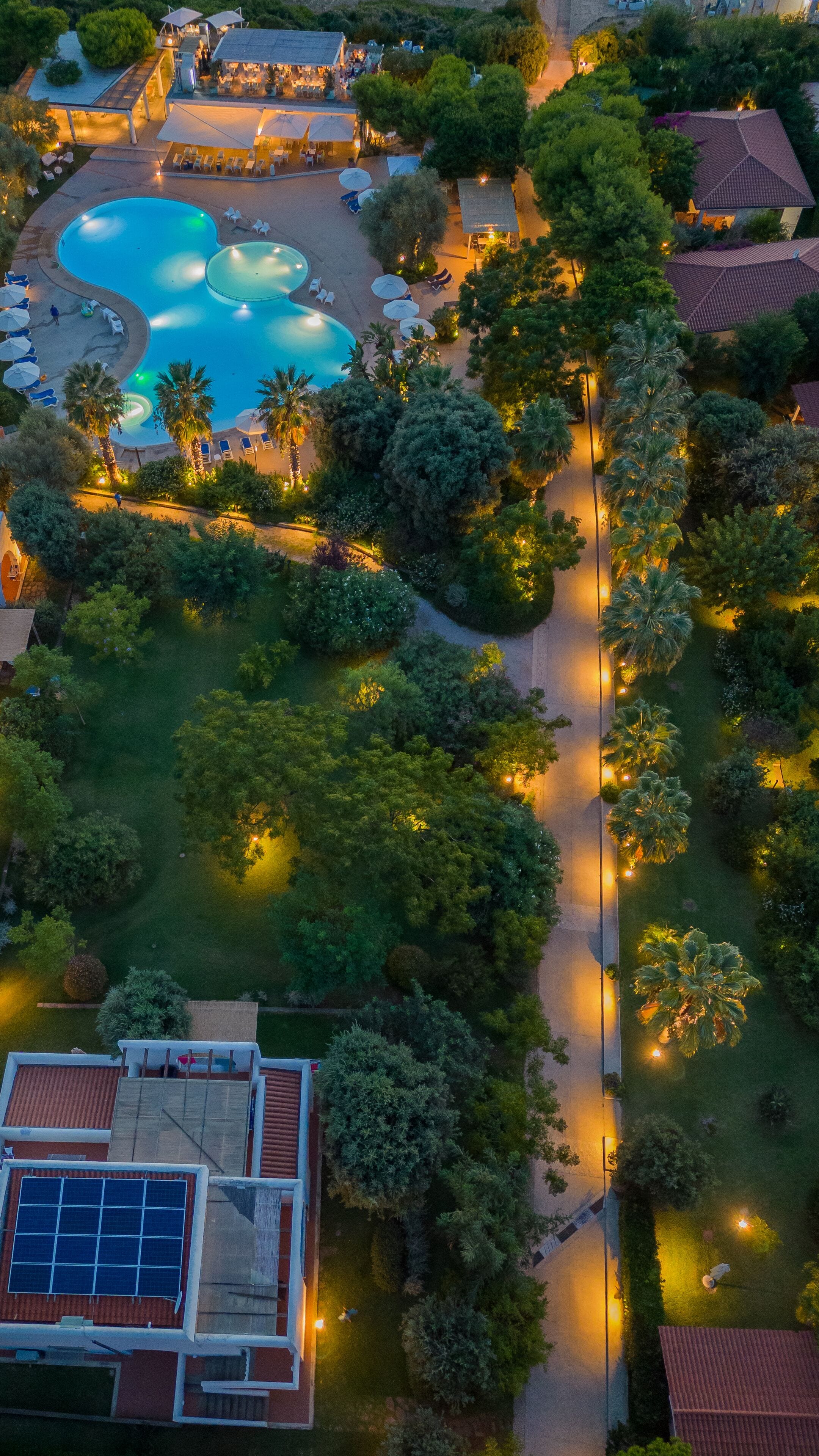 Vista aérea de un complejo turístico con múltiples piscinas, una cancha de tenis y zonas verdes circundantes.