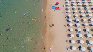 Une vue aérienne d’une plage avec une eau cristalline, des parasols et des personnes.