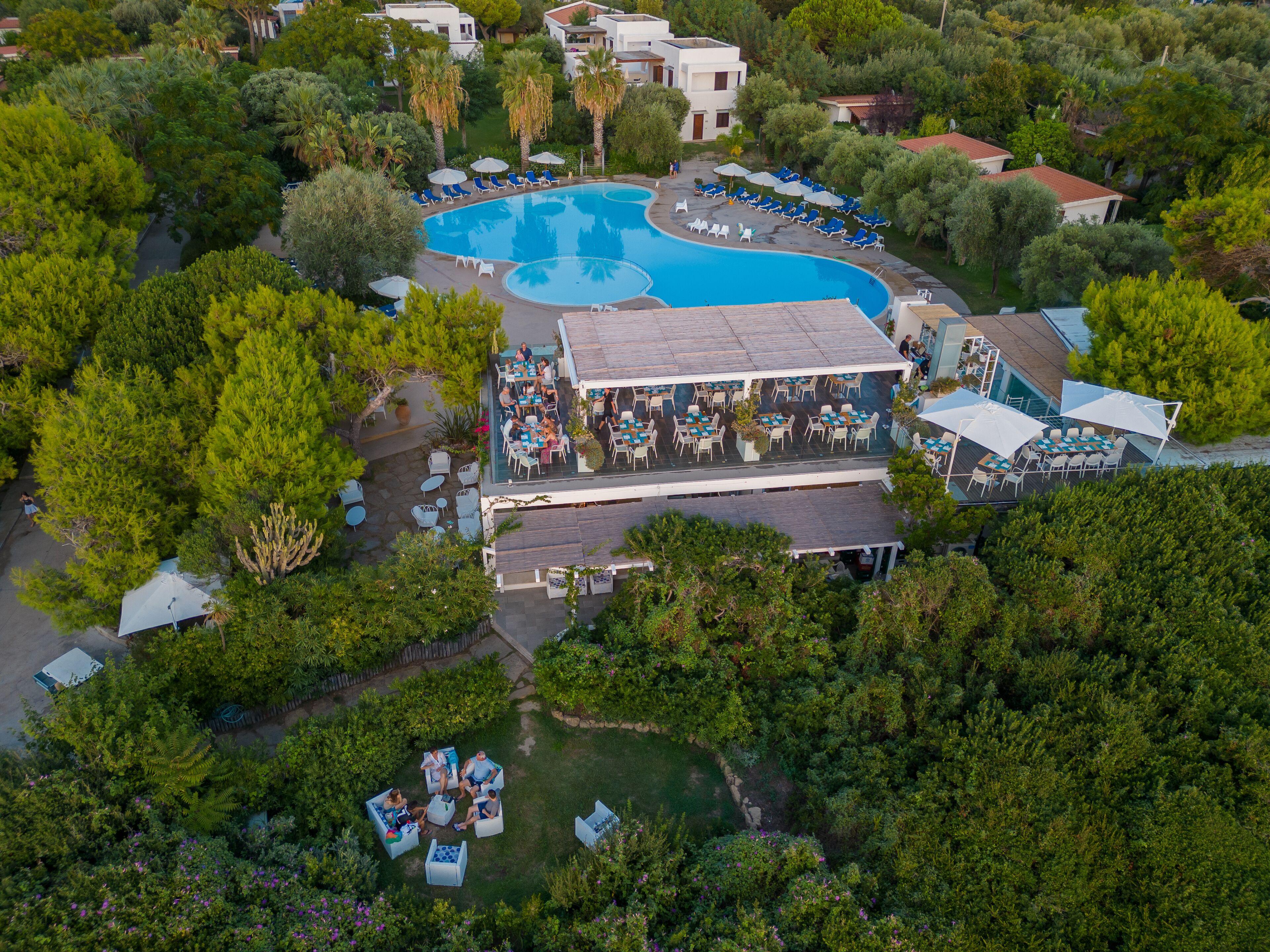 Vista aérea de un complejo turístico con una amplia piscina, zonas de estar al aire libre y exuberante vegetación.