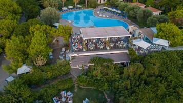 Vista aérea de um resort com uma grande piscina, áreas de estar ao ar livre e vegetação exuberante.