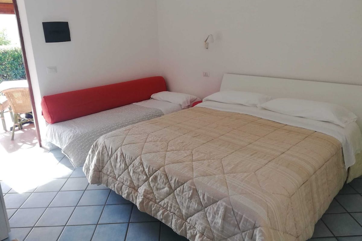 Une chambre avec deux lits, l’un doté d’une tête de lit rouge et l’autre d’une tête de lit blanche. Il y a une petite table et une chaise à l’extérieur de la chambre.