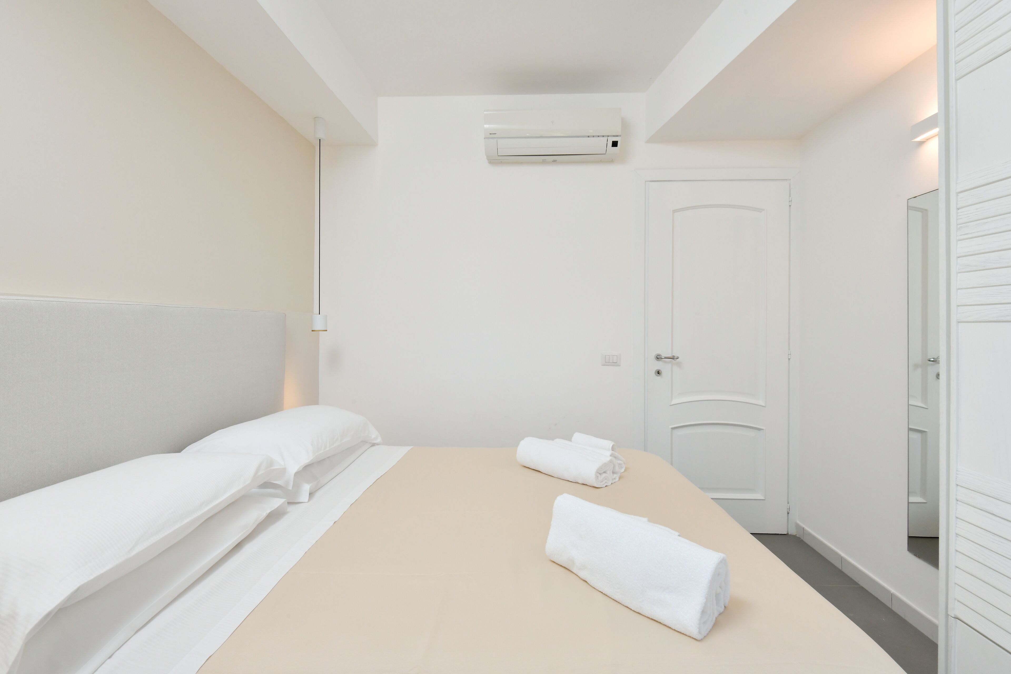 A hotel room with a bed, a door, and an air conditioning unit.