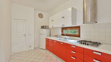 Une cuisine moderne avec des meubles blancs et rouges, une cuisinière à gaz, un four à micro-ondes et une fenêtre au-dessus de l’évier.