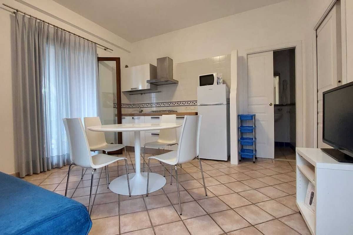 Une chambre d’hôtel de taille réduite, comprenant une table et des chaises, un coin cuisine, une télévision et un lit.