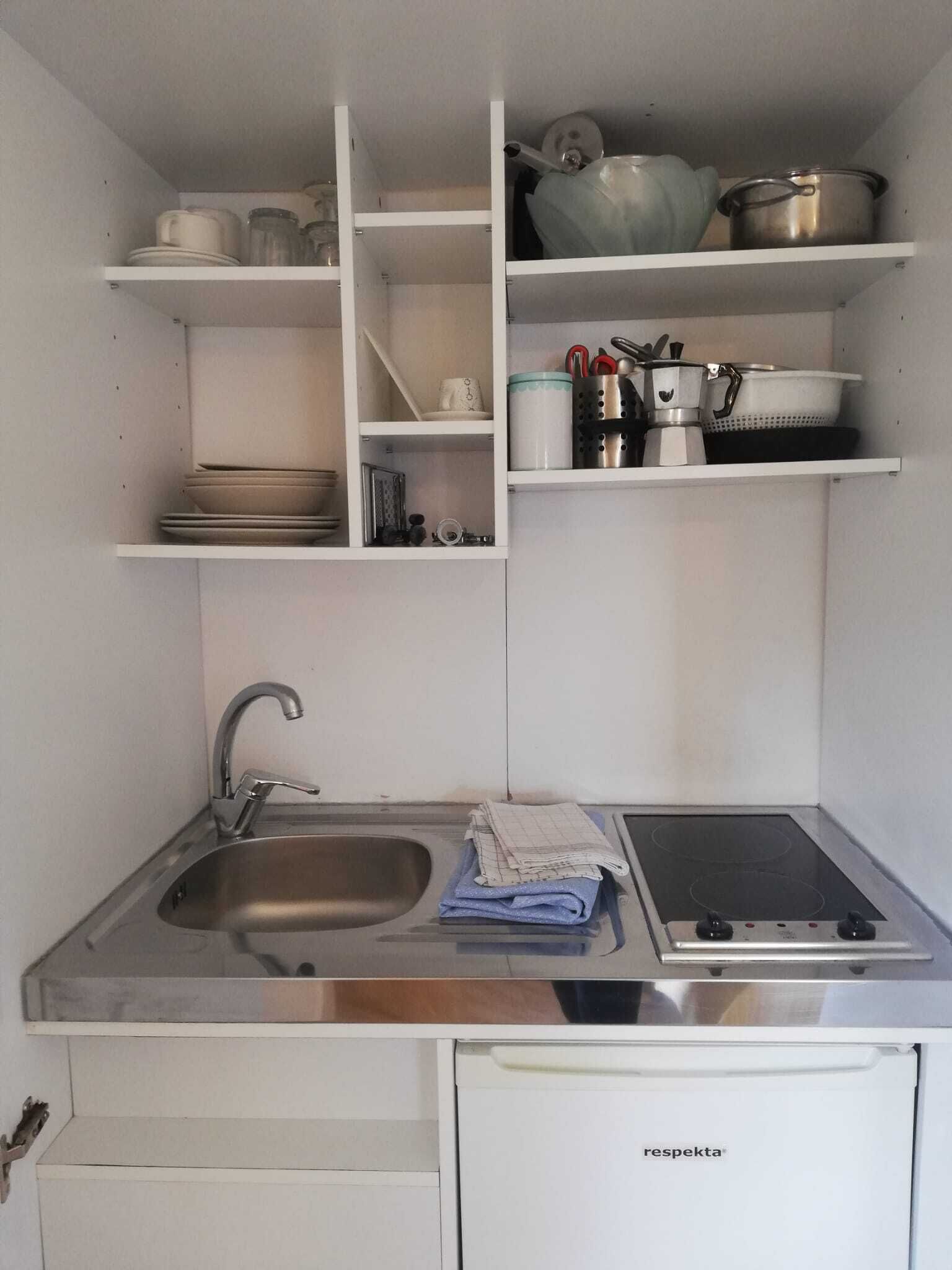 Et lille køkken med vask, komfur og opbevaringshylder.