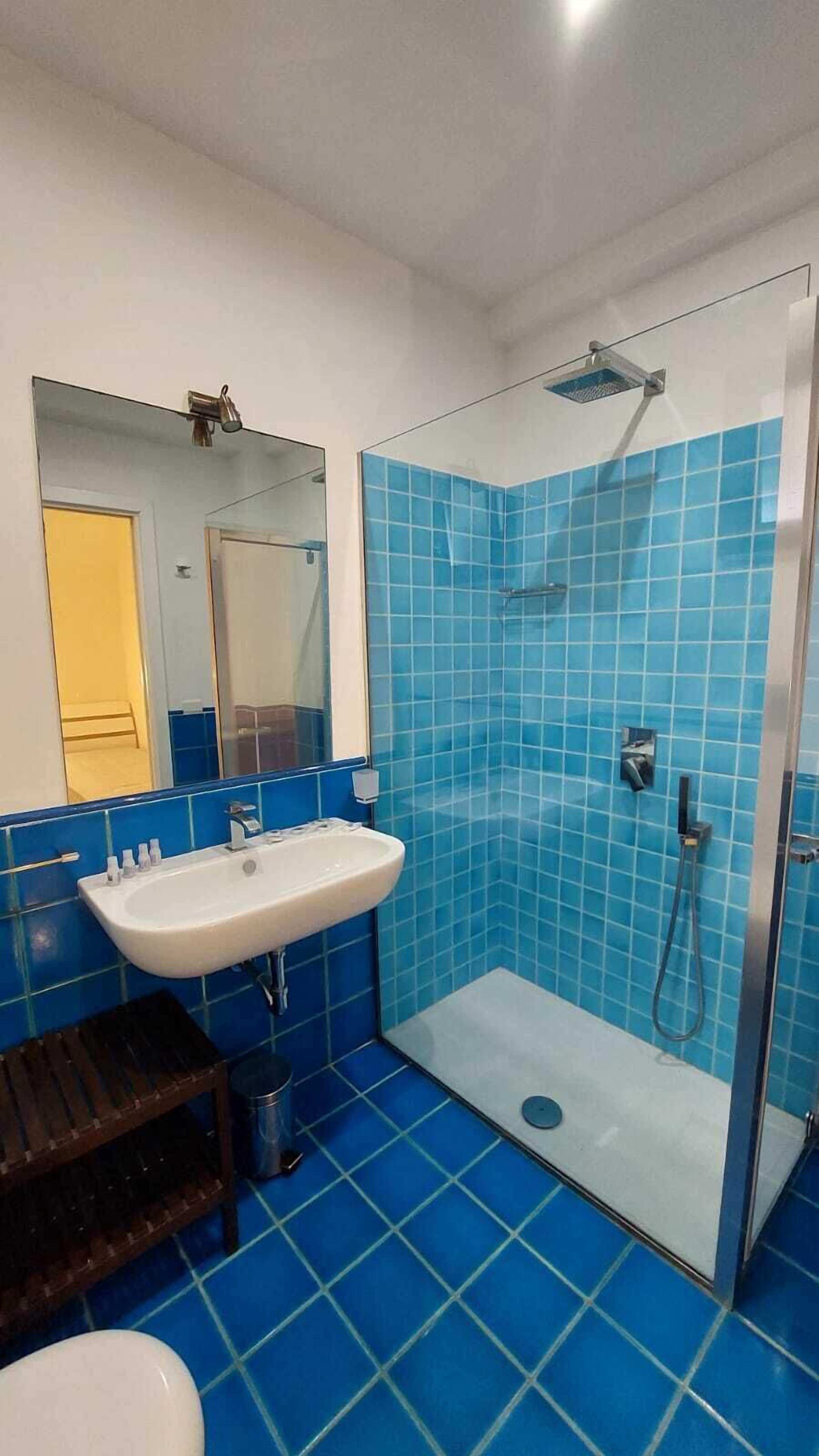 A bathroom with a glass-enclosed shower, a white sink, and blue-tiled walls.
