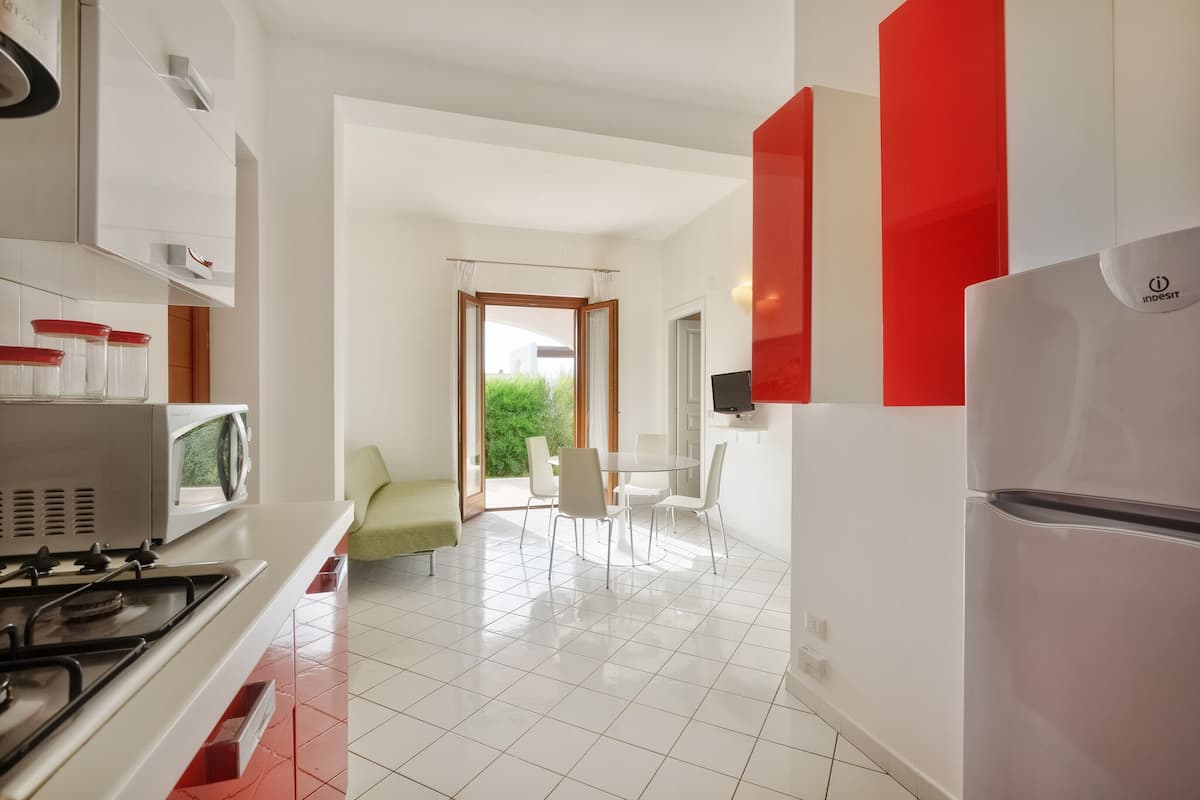 Une cuisine moderne avec des meubles blancs, un réfrigérateur rouge et un coin repas avec des chaises blanches.
