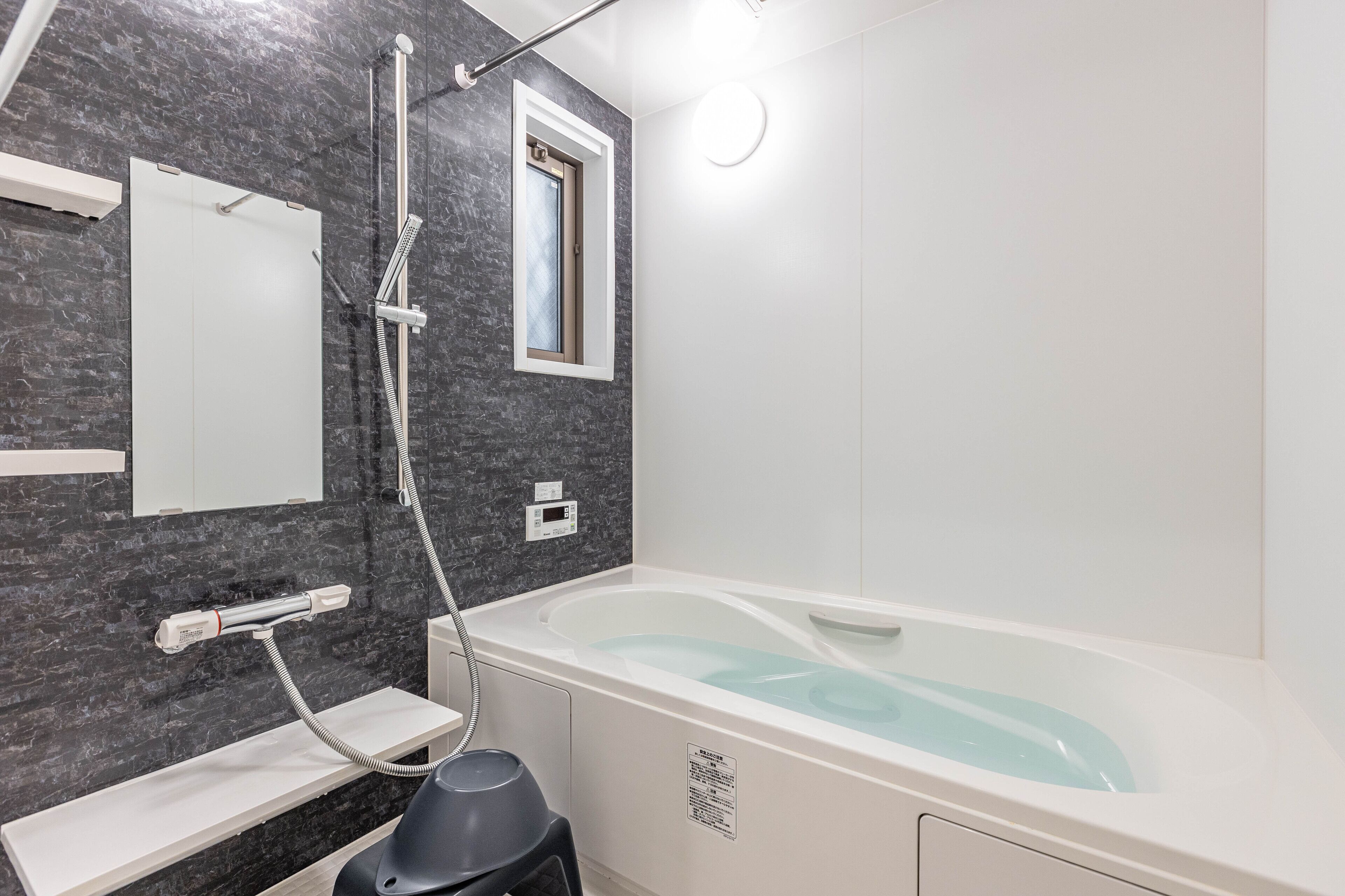 A modern bathroom with a bathtub, a shower, a vanity with a mirror, and a small window.