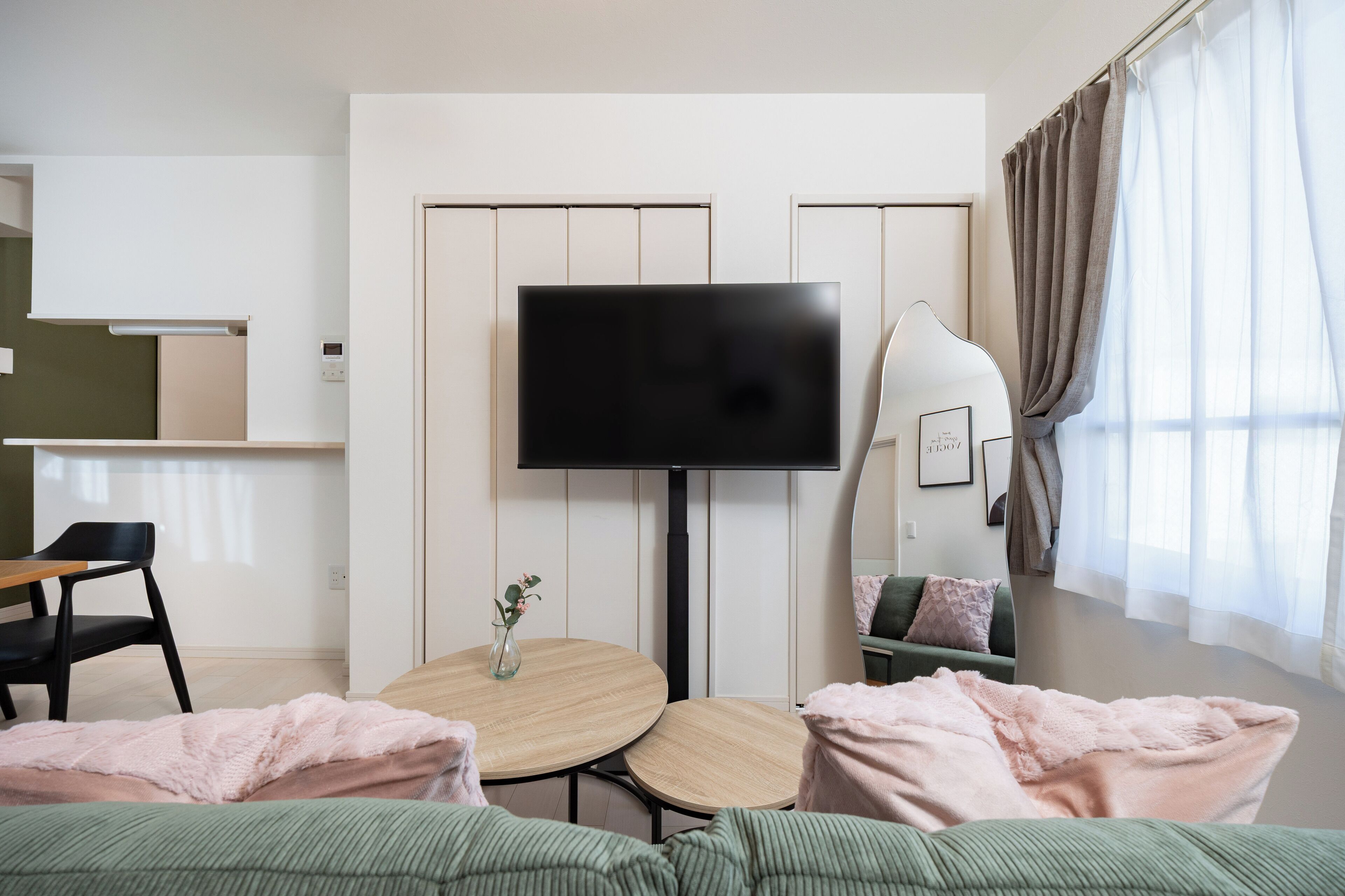 Habitación de hotel moderna con televisor de pantalla plana, una mesa redonda de madera, un sofá verde y un espejo grande.