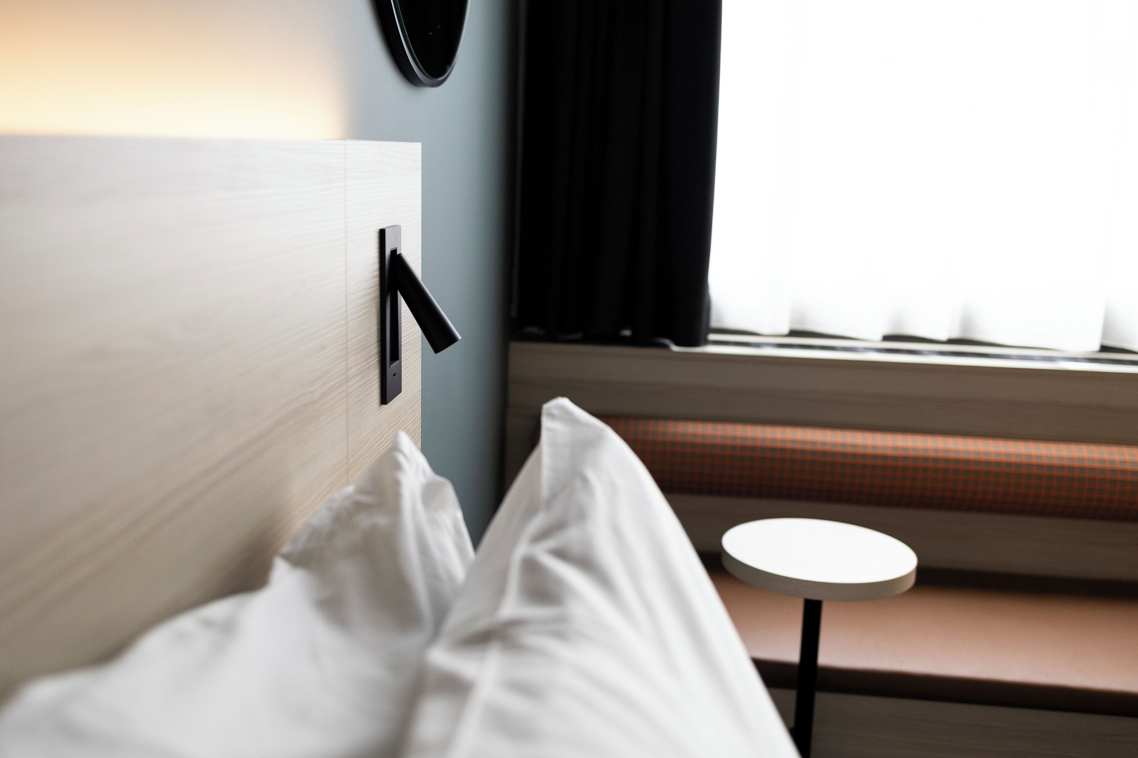 Una habitación de hotel con una cama, una mesa redonda y un ventanal con cortinas.