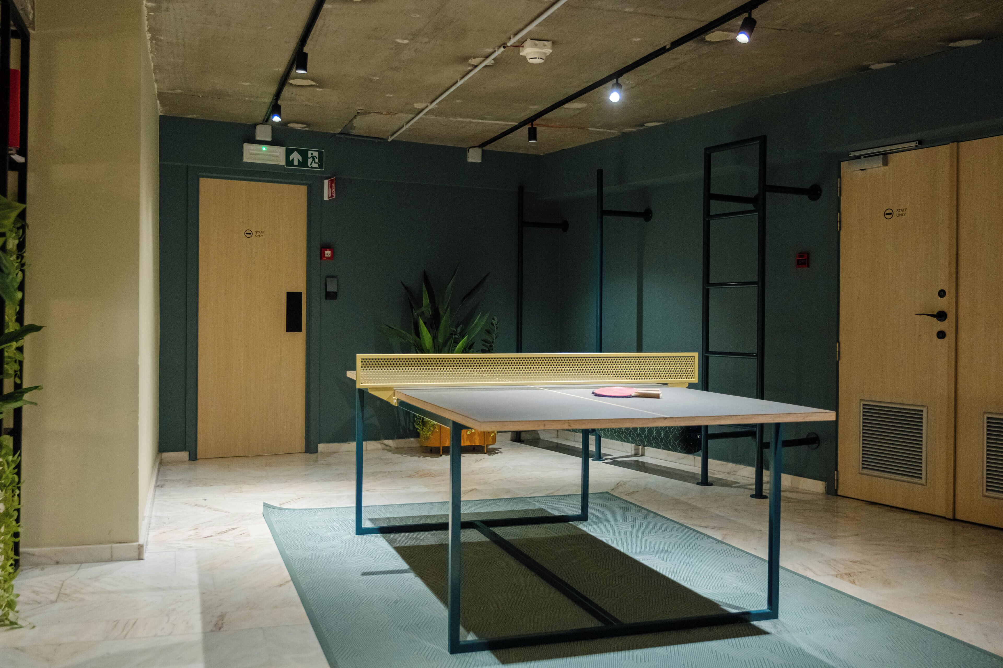 Una habitación con mesa de ping pong, una puerta, una planta y una escalera fijada a la pared.