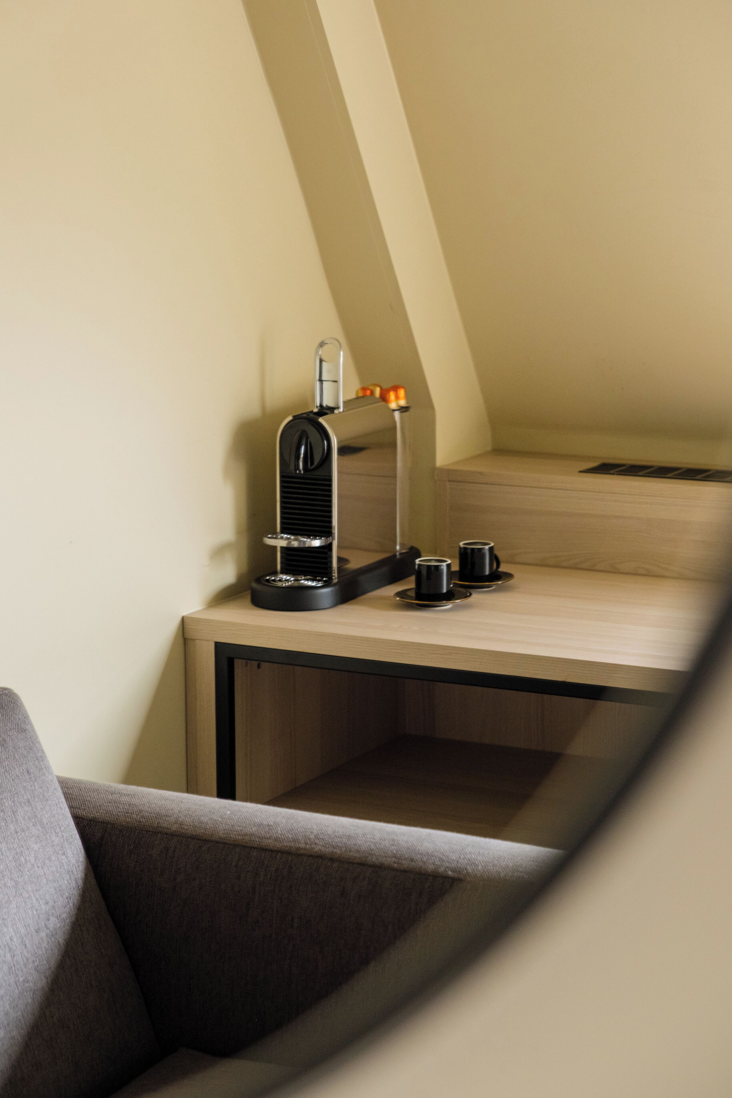 A small, modern kitchenette with a coffee machine, two cups, and a lamp.