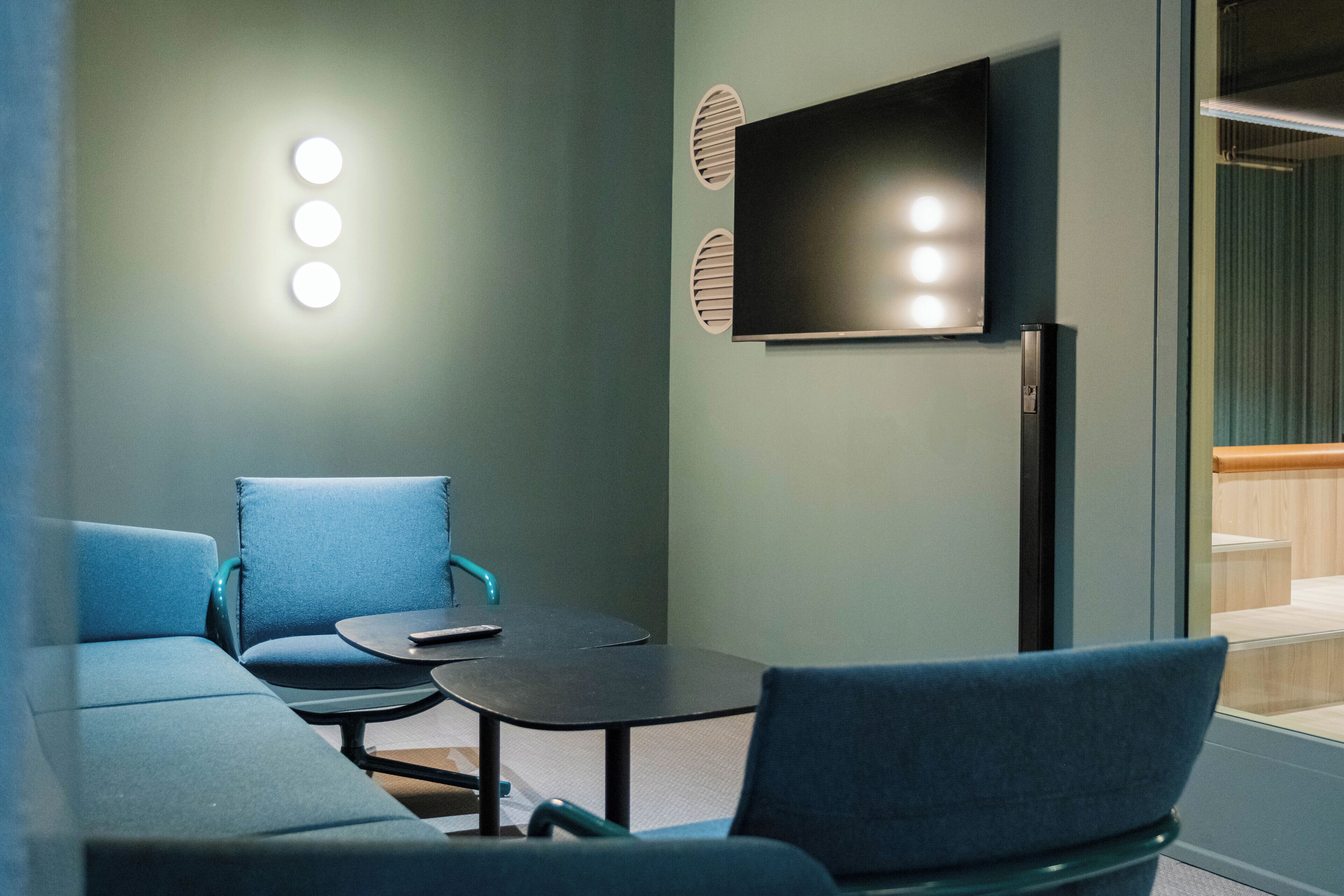 A modern waiting area with a sofa, chairs, a small table, and a flat-screen TV mounted on the wall.