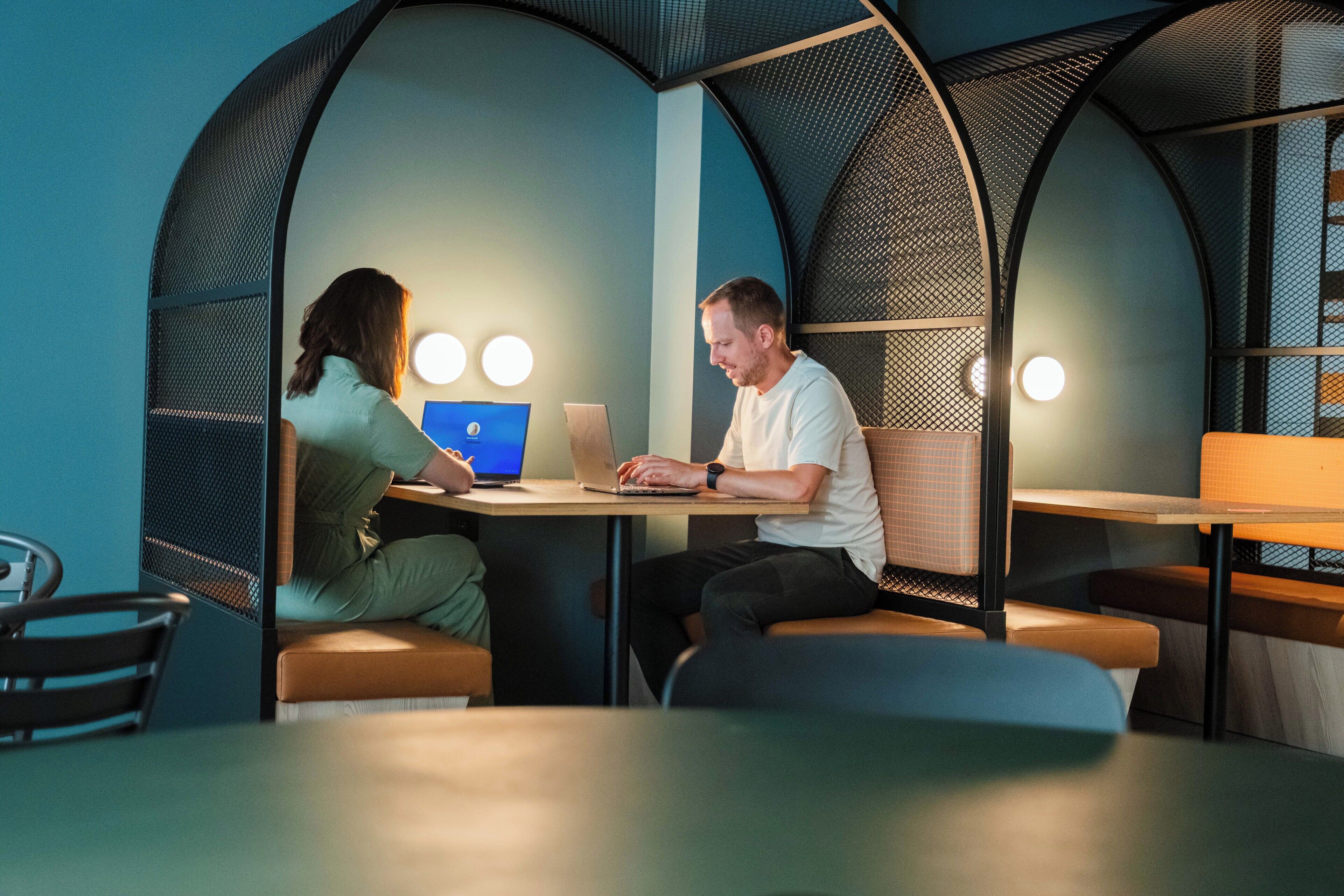 A modern workspace with two people at a table, laptops, and a lamp.