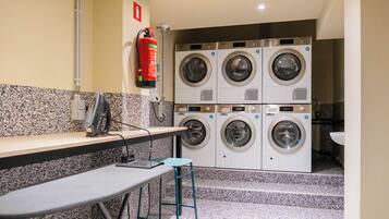 A laundry room with four washing machines, a fire extinguisher, a table, and a chair.
