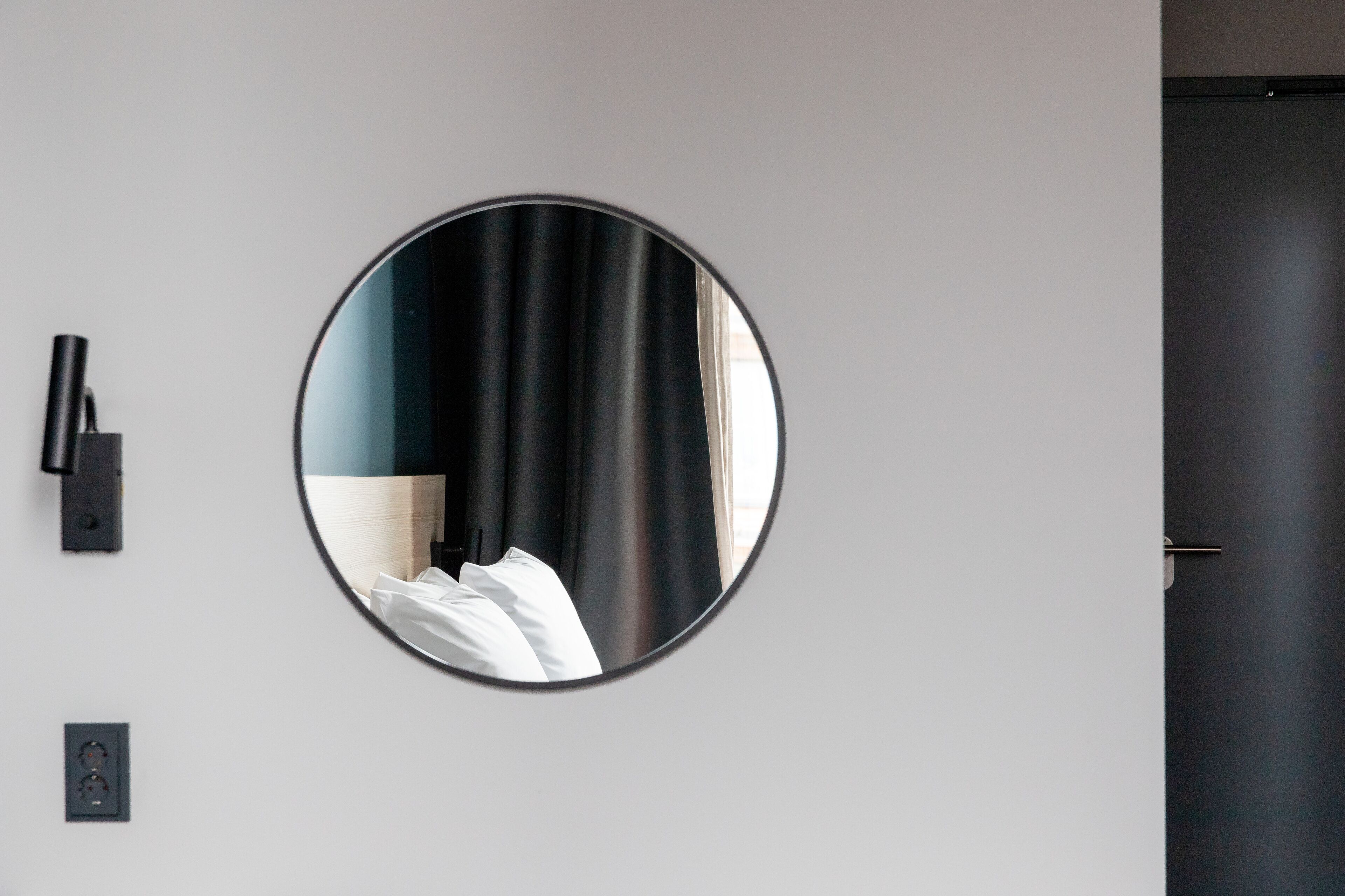 A round mirror on a wall, a black door, and a light switch.