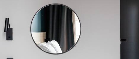 A round mirror on a wall, a black door, and a light switch.