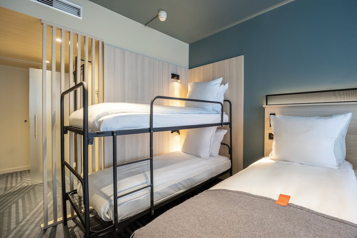 A bunk bed room with a headboard, a bedside table, and a wall-mounted light.