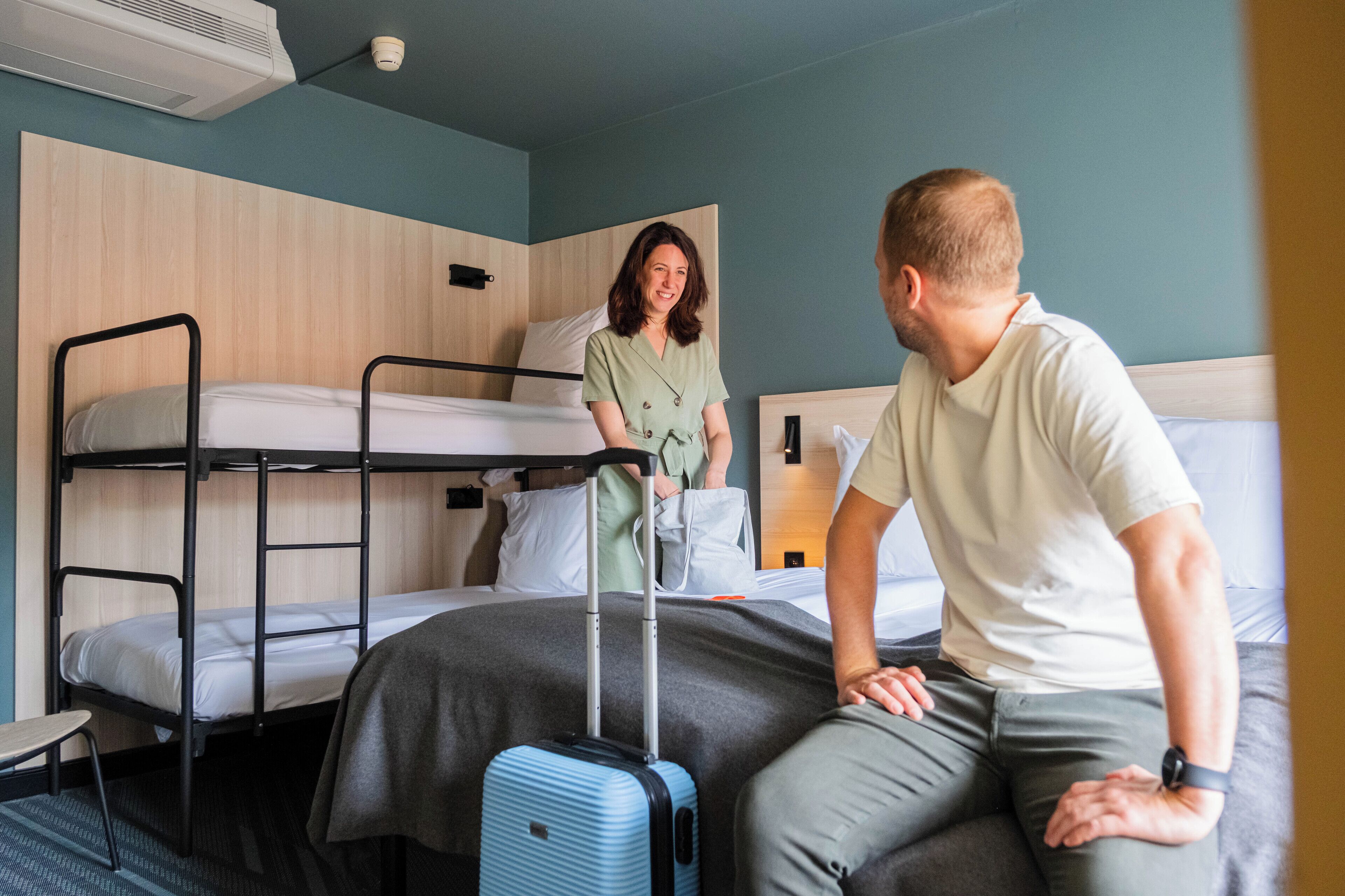 A hotel room with bunk beds, a suitcase, and a person sitting on the bed.