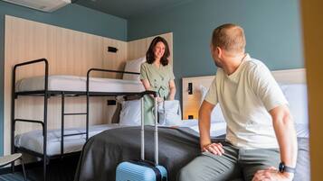Een hotelkamer met stapelbedden, een koffer en een persoon die op het bed zit.