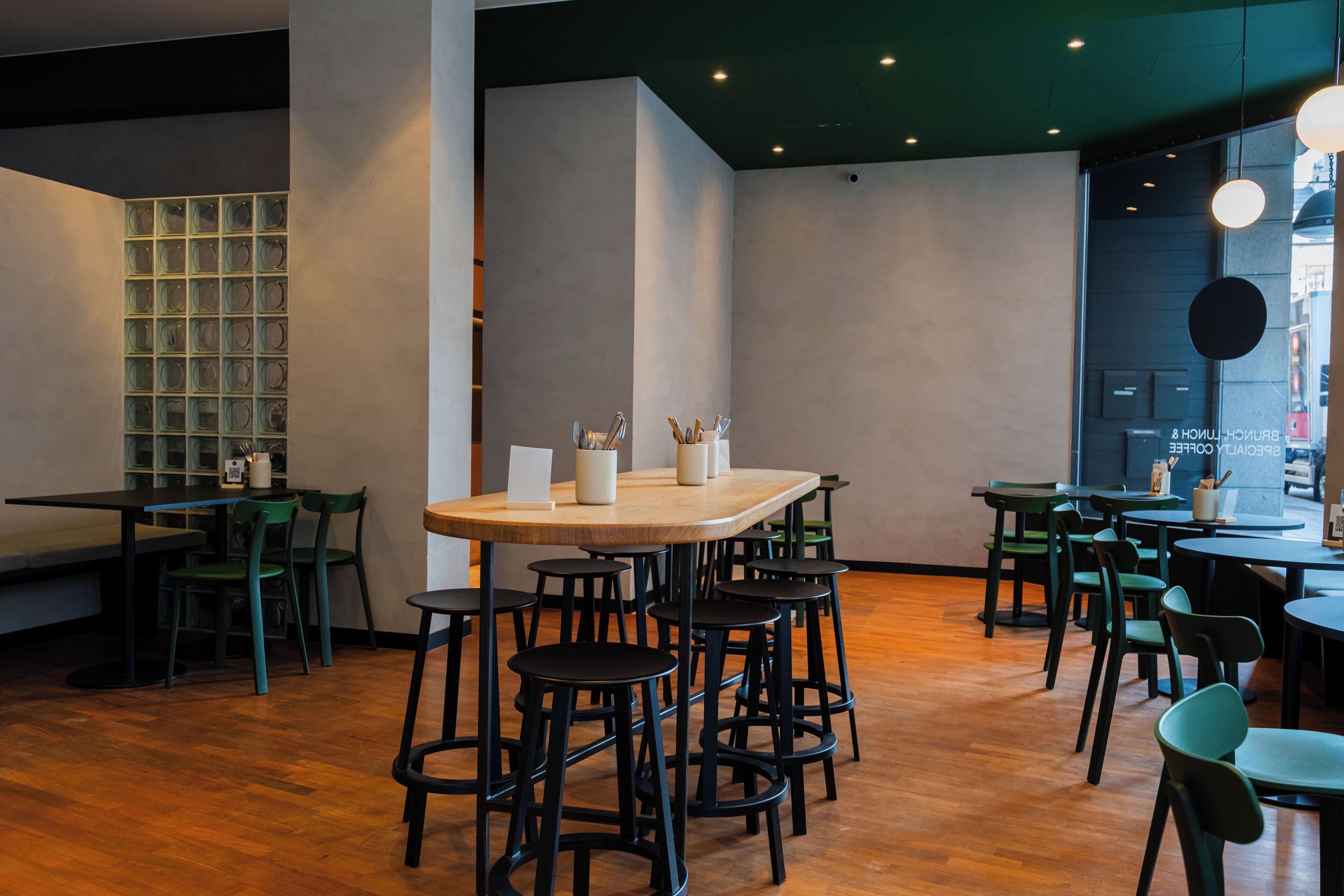 A modern restaurant interior with round tables, bar stools, and green chairs.