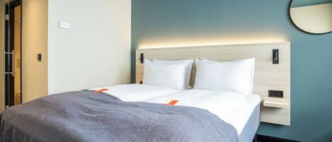 Una habitación de hotel con una cama, una mesita de noche, un espejo en la pared y una puerta.