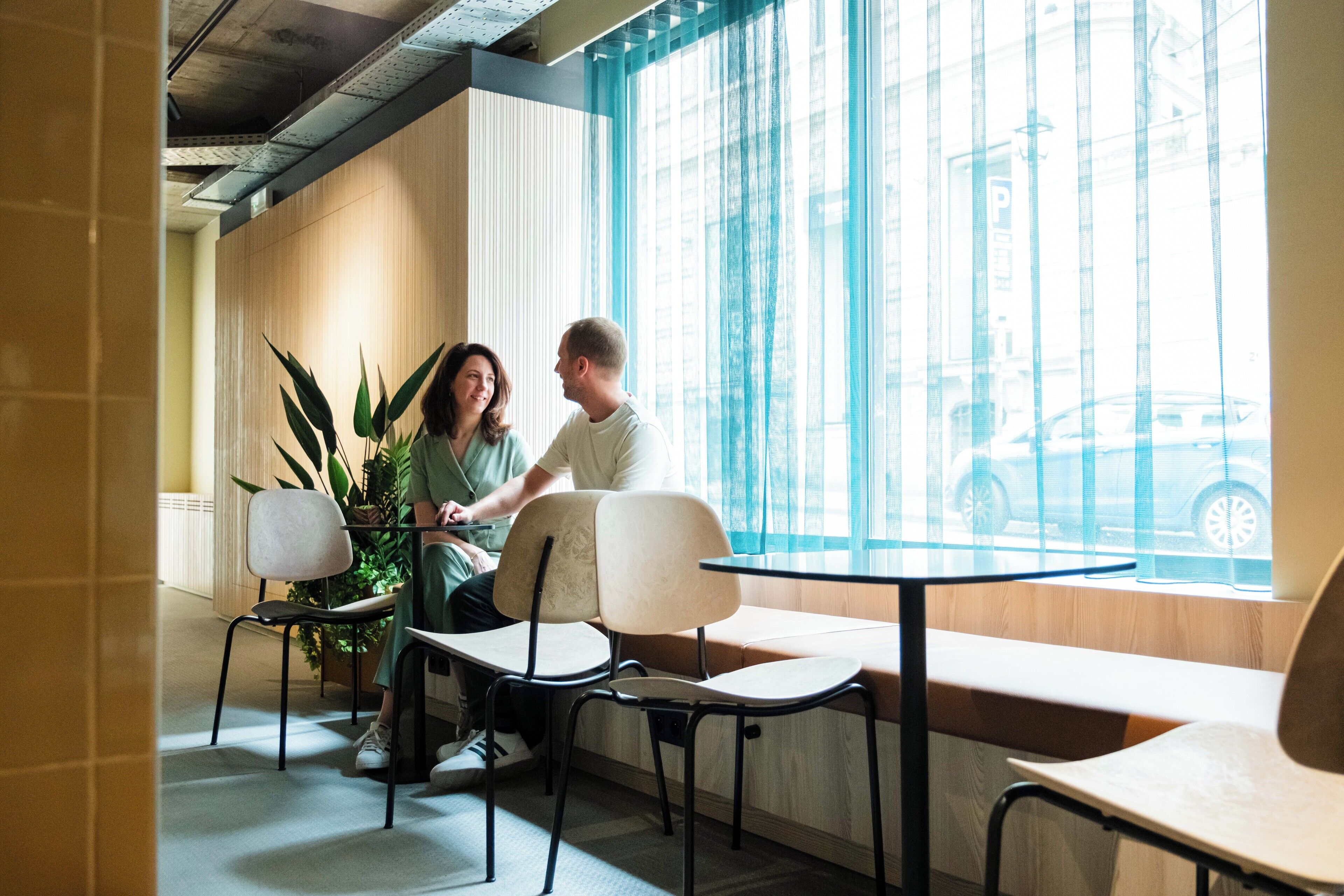 A modern indoor seating area with tables and chairs, large windows with blue curtains, and a view of the street outside.