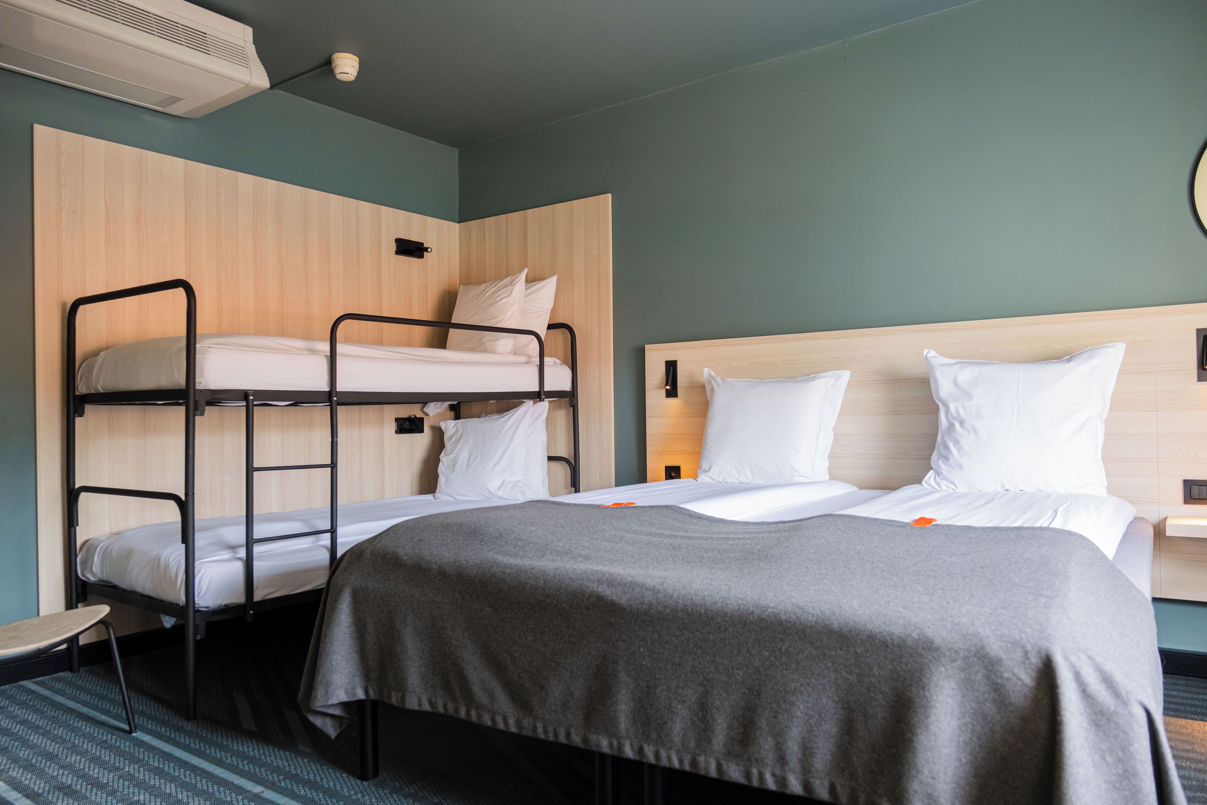 Une chambre d’hôtel équipée d’un lit superposé, d’un lit simple, d’une table de chevet et d’un climatiseur fixé au mur.