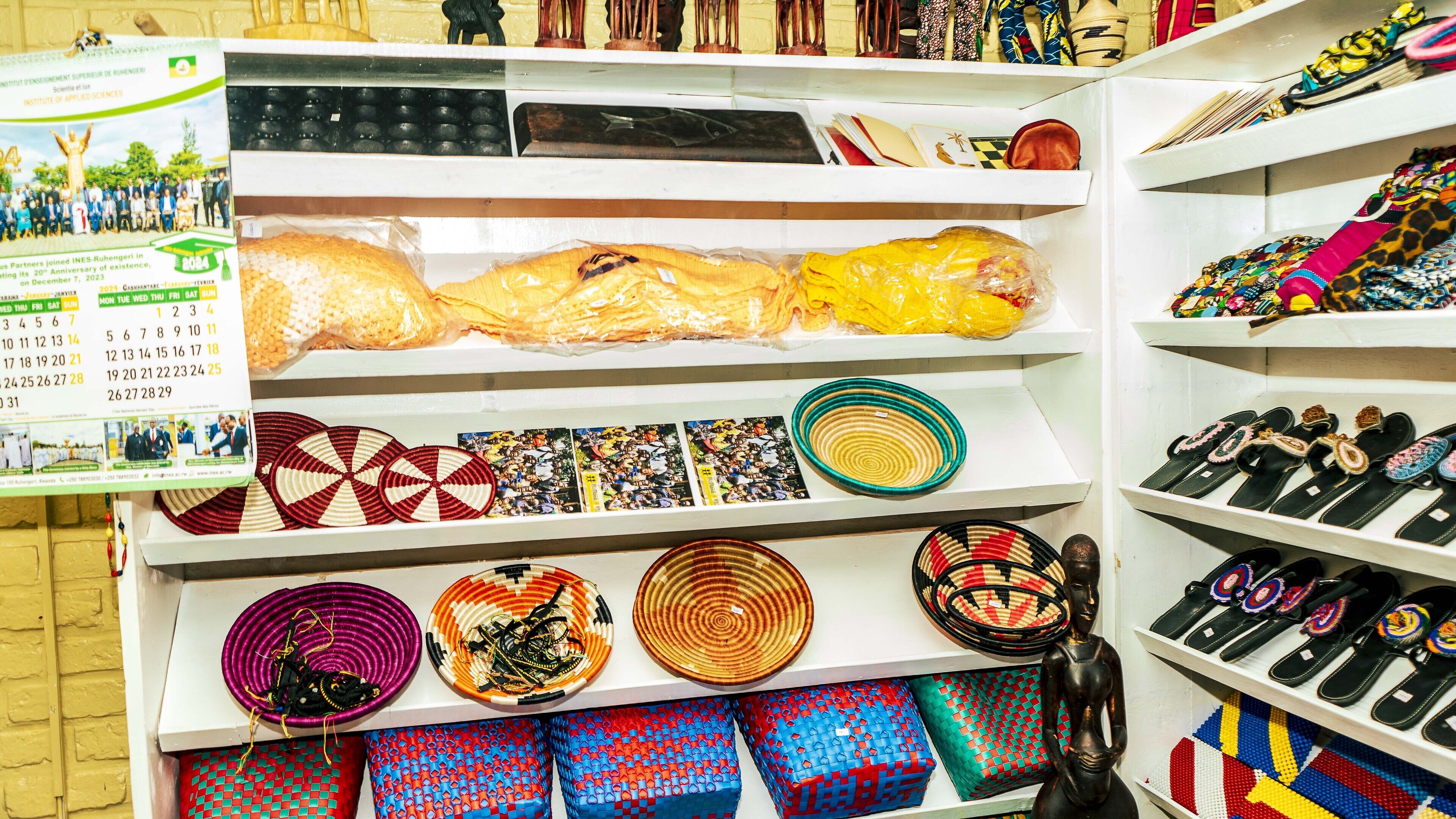 A store with shelves displaying various items including woven baskets, colorful textiles, and shoes.