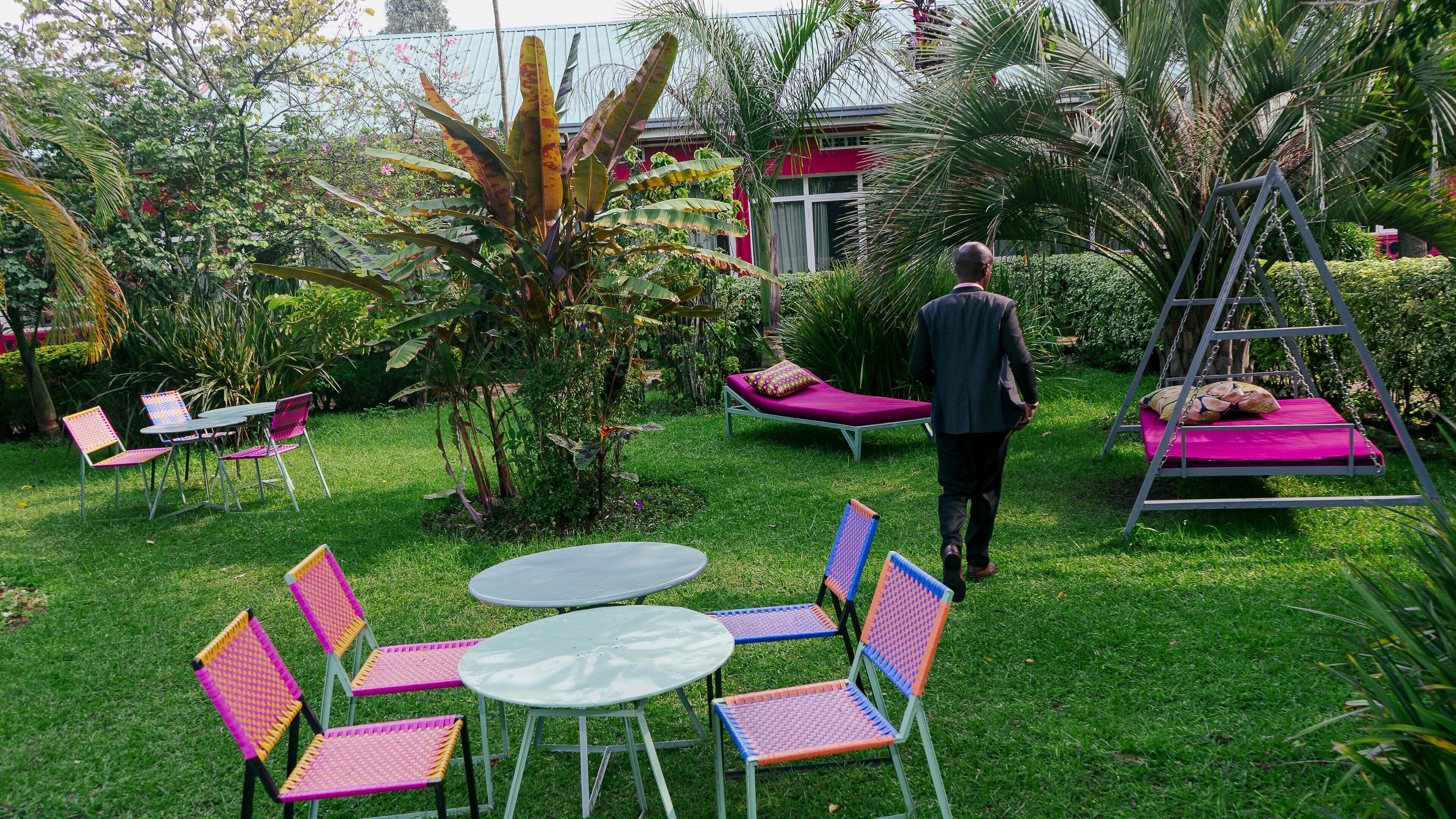 An outdoor garden area with a grassy lawn, several colorful chairs, a small round table, and a swing set.