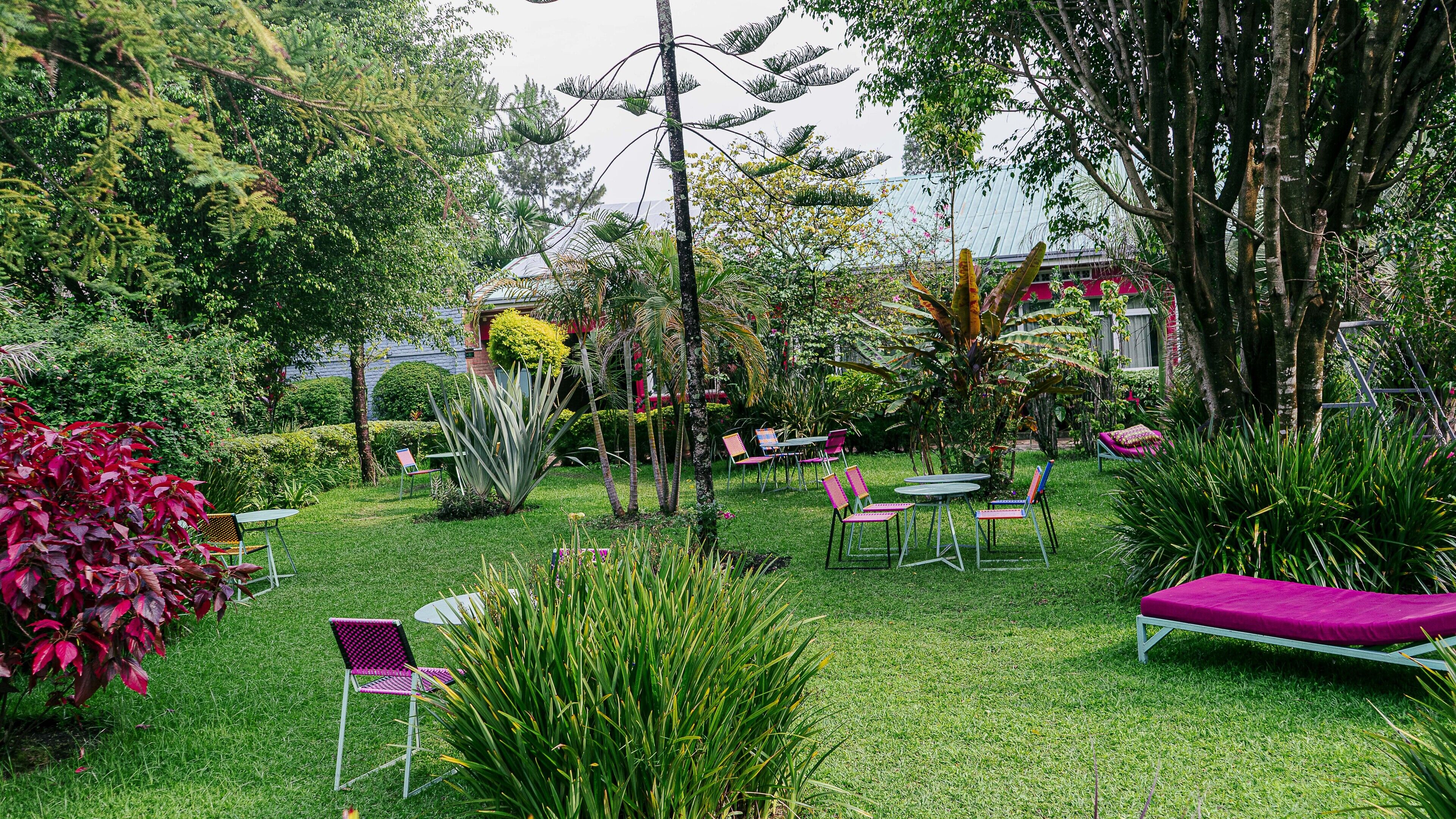 Un exuberante jardín con mobiliario exterior, mesas y sillas, rodeado de plantas y árboles.