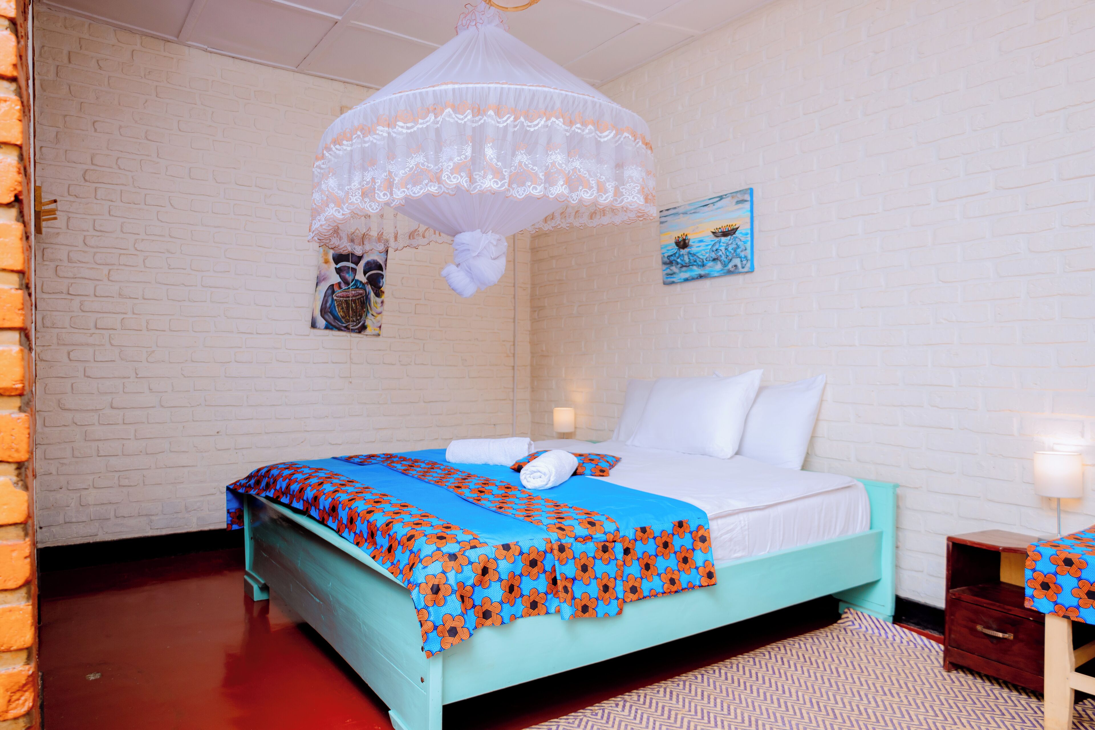 Un dormitorio con una cama, una mesita de noche, una lámpara, un cuadro en la pared y una pared de ladrillo.