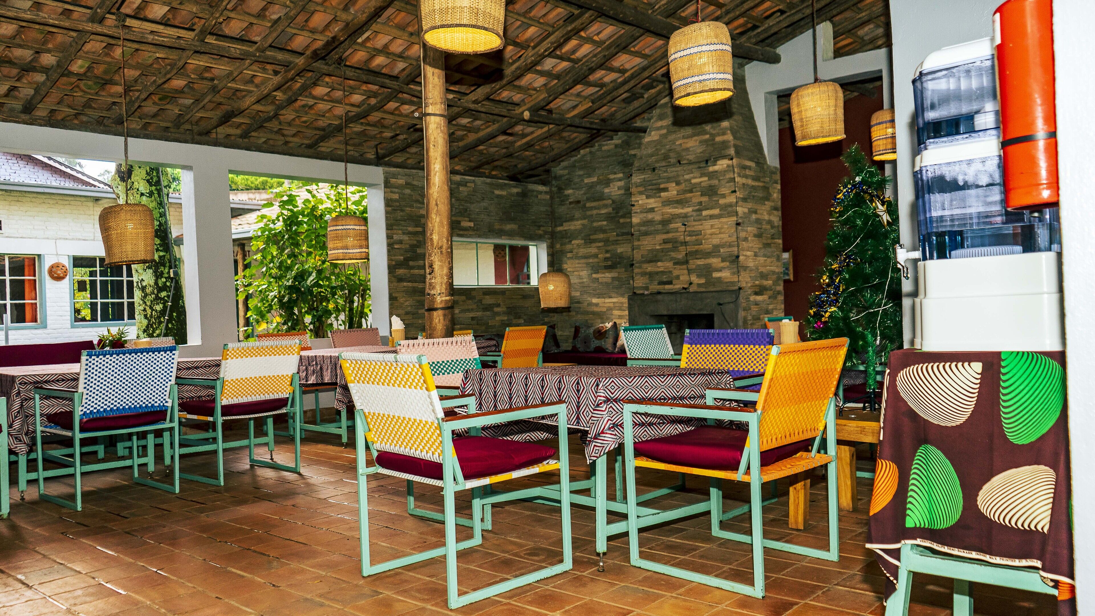 Un restaurante con mesas al aire libre, lámparas colgantes de mimbre y un árbol de Navidad.
